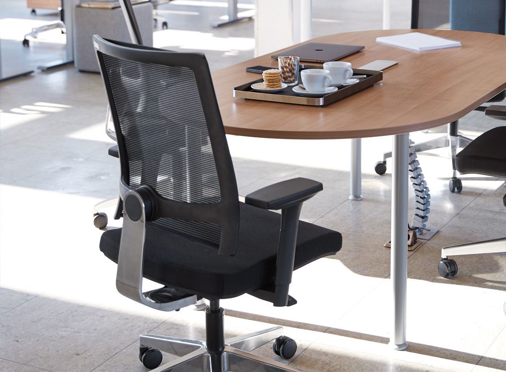 Ergonomische vergaderstoel en vergadertafel met koffiekopjes en koekjes.