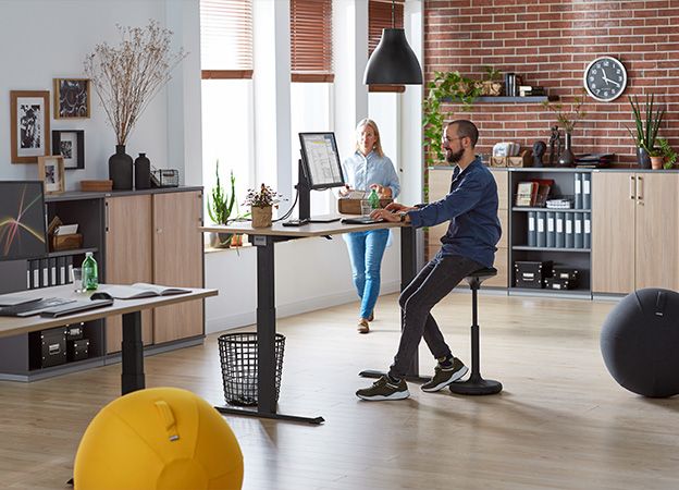 Mann arbeitet mit ergonomischer Stehhilfe rückenschonend im Büro