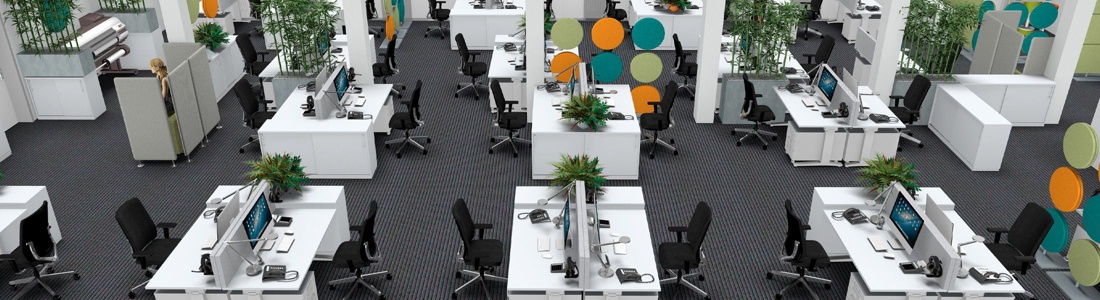 Een open kantoorruimte met verschillende witte bureaus die telkens per 2 tegenover elkaar staan en zwarte bureaustoelen. Op strategische plaatsen staan akoestische wanden en kasten.