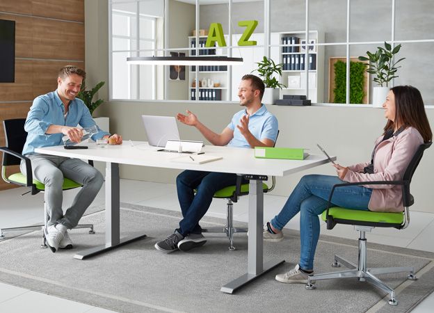 Drei Mitarbeiterinnen und Mitarbeiter im Meeting an einem modernen Bürotisch mit ergonomischen Drehstühlen in einem offenen Arbeitsbereich.