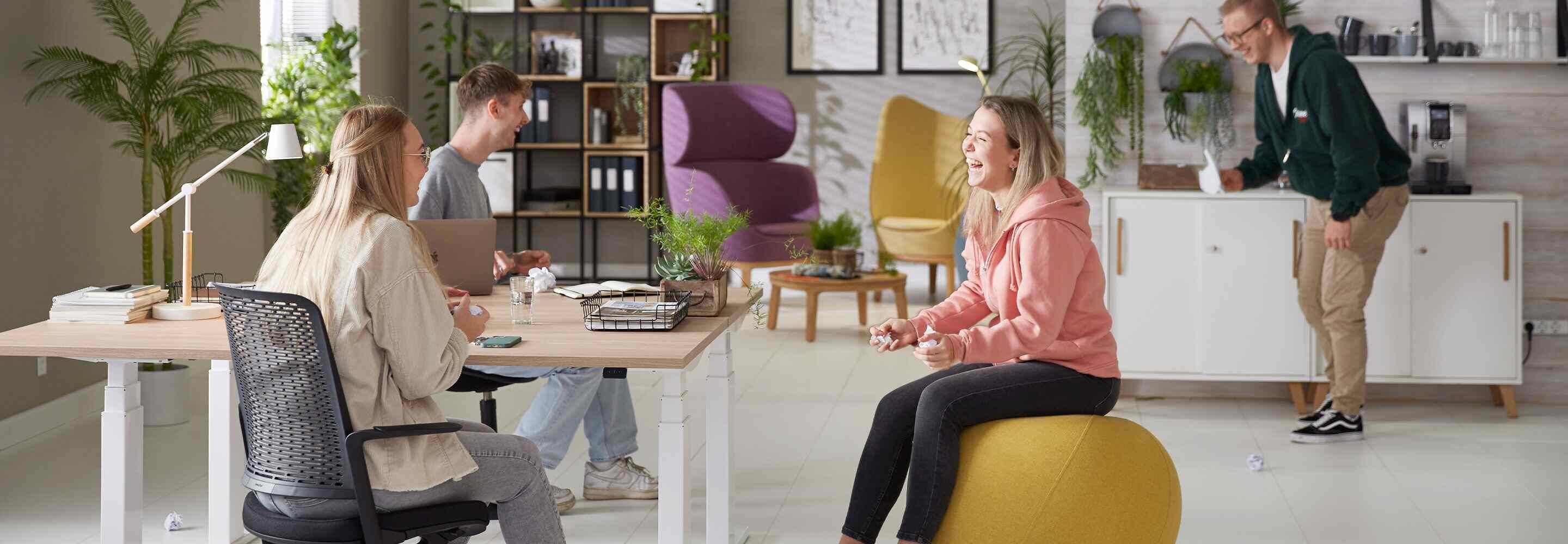 Vier junge Menschen sitzen lachend in einem Büro.