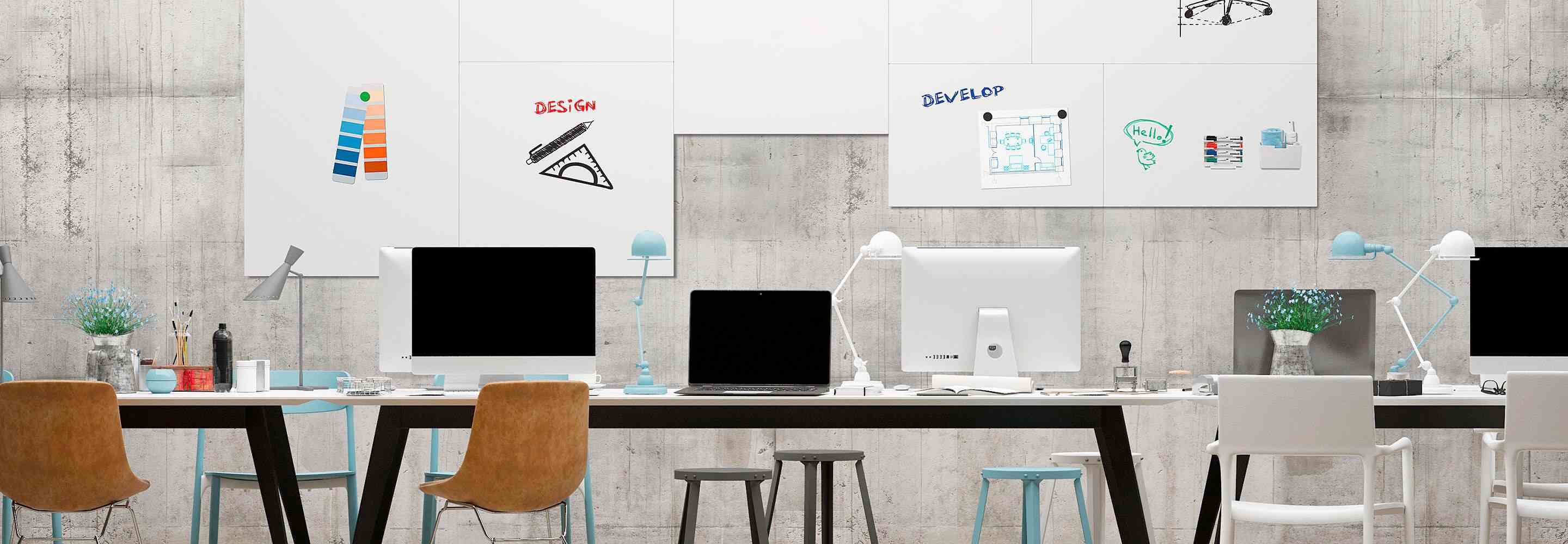 Verschillende bureaus staan naast elkaar voor een muur waarop whiteboards zijn bevestigd. Op de whiteboards staan schetsen en plannen.