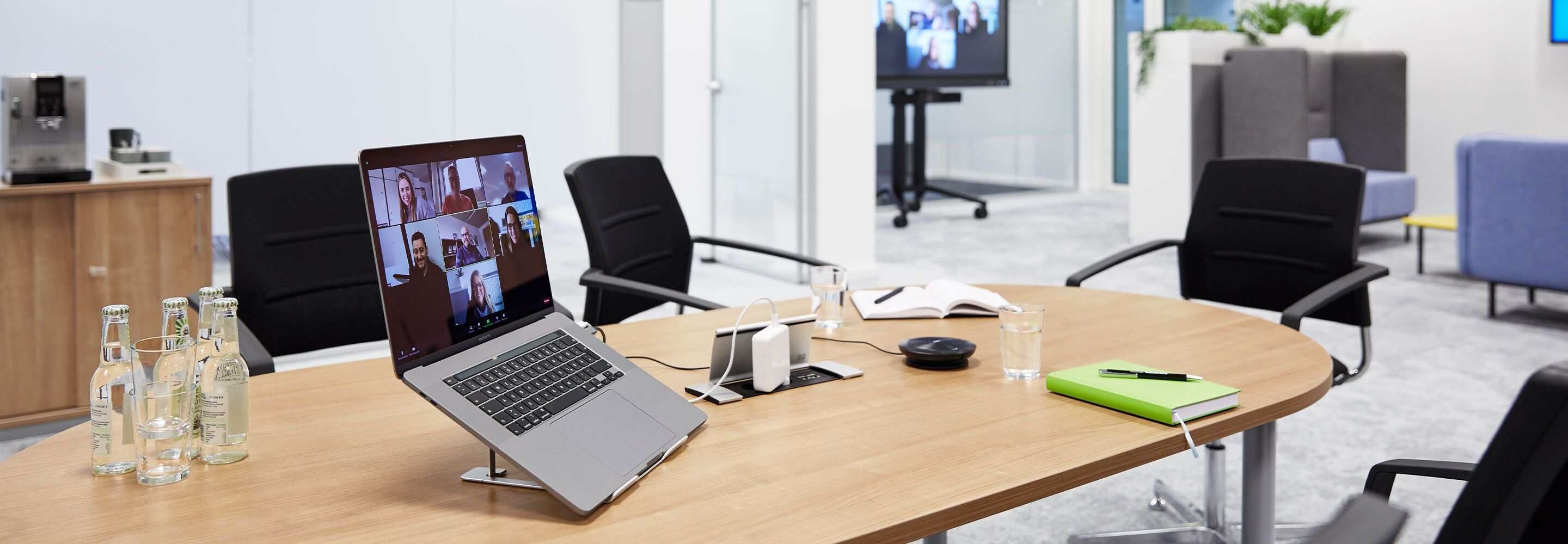 Een laptop met een geopende videoconferentie staat op een vergadertafel.