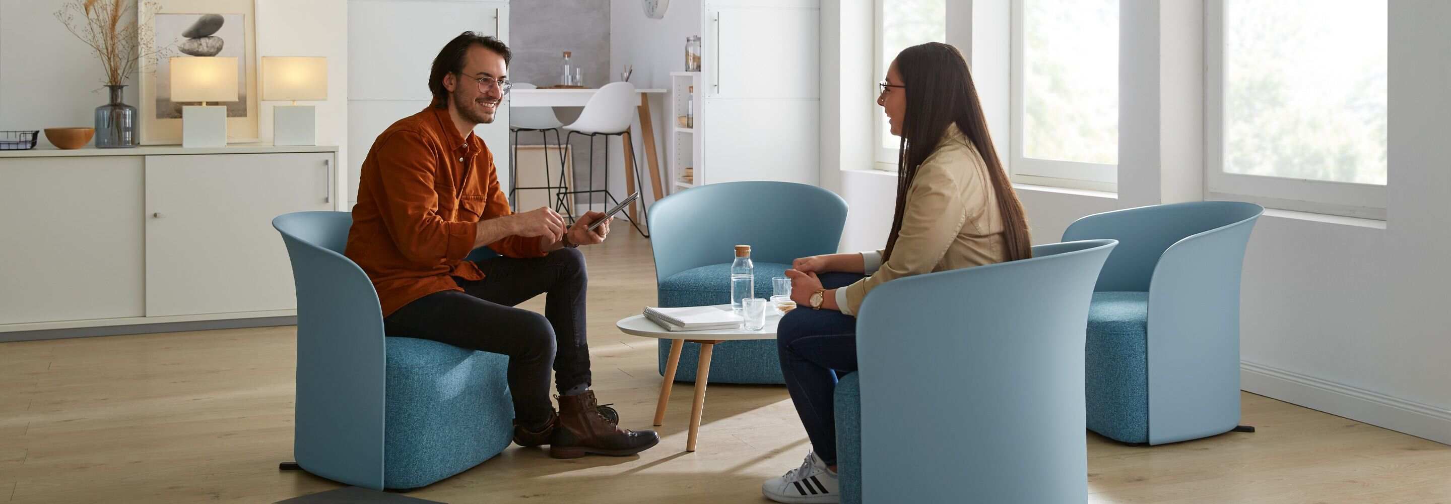 Ein Mann und eine Frau sitzen in Sesseln an einem kleinen Tisch und unterhalten sich.