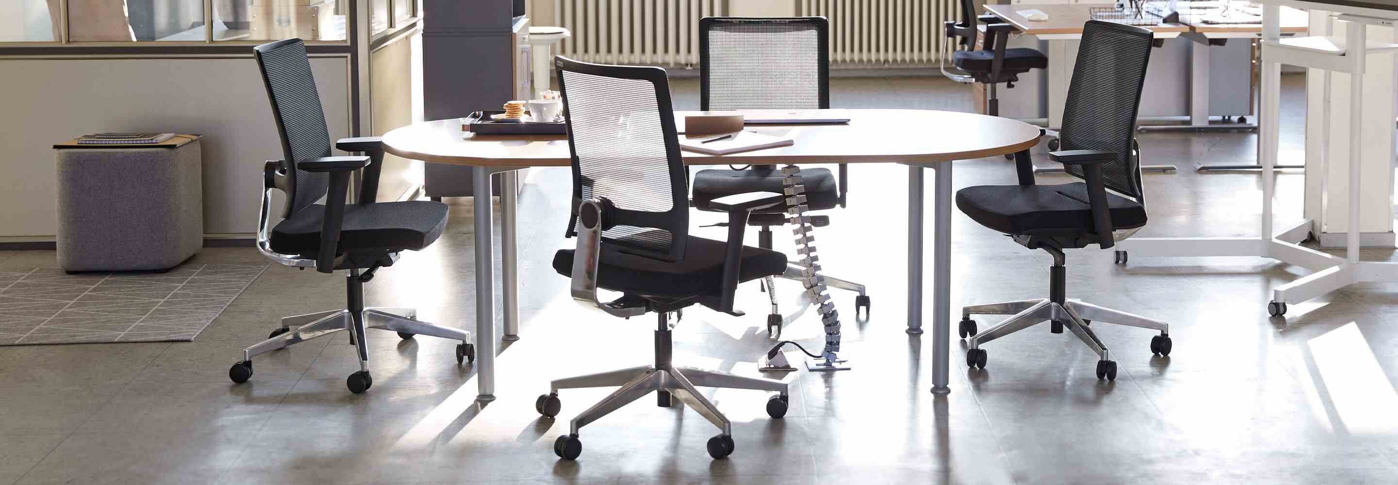 Aan een kantoortafel zie je vier lege bureaustoelen.