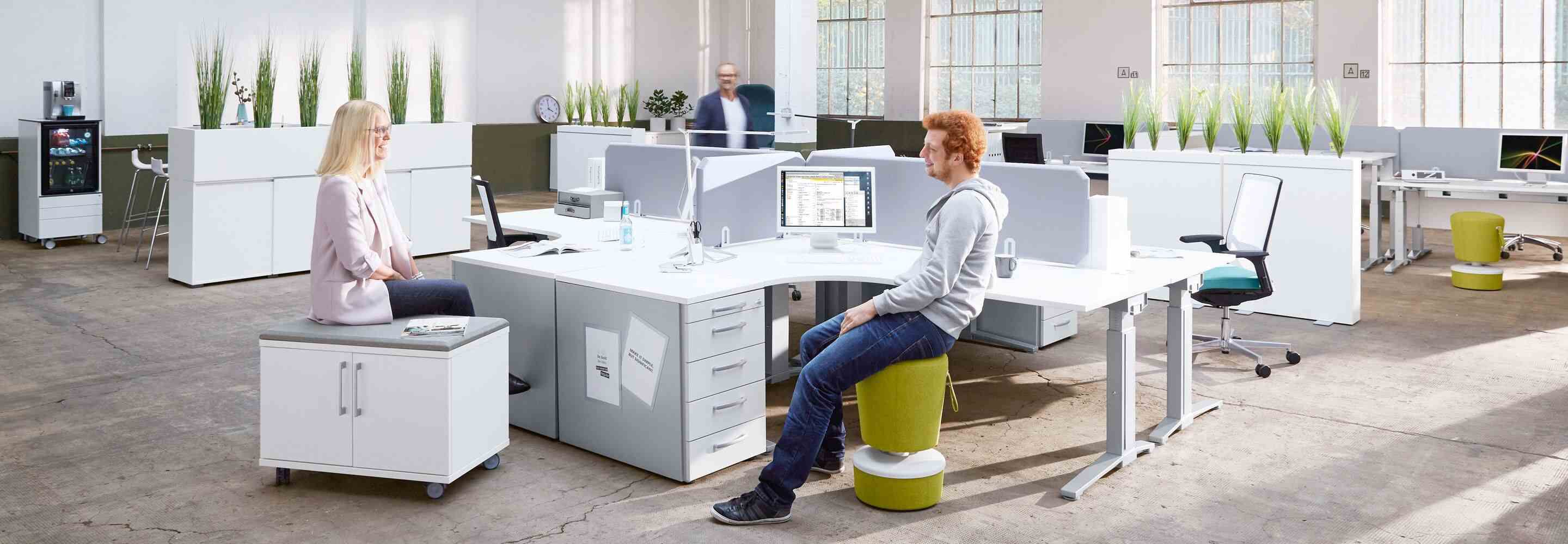 Een vrouw en een man zitten ontspannen rond een bureau en praten.