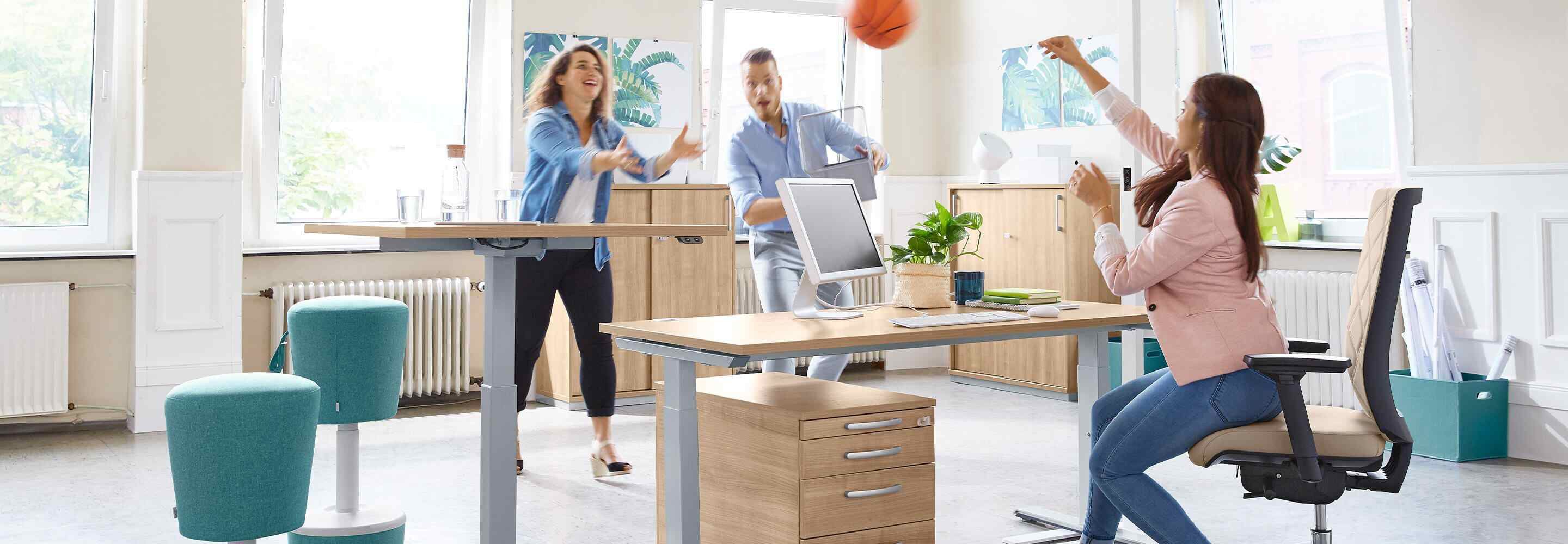 Twee vrouwen en een man gooien een basketbal naar elkaar op kantoor.