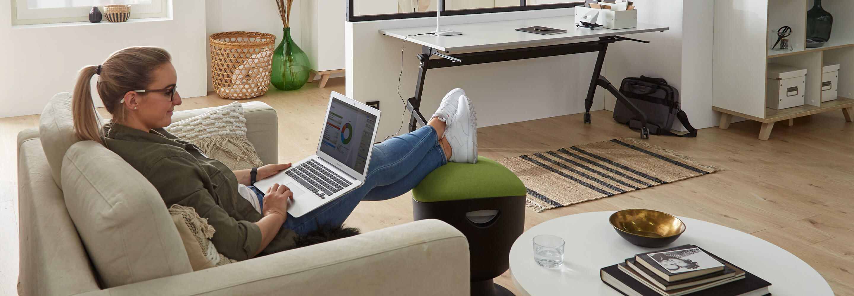 Een vrouw zit op de bank met haar laptop op haar schoot.