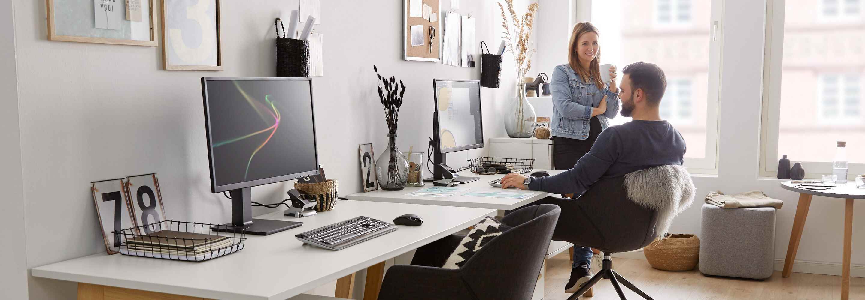 Een vrouw en een man zitten in een kantoor. De vrouw leunt met een kopje tegen het bureau, de man zit op zijn bureaustoel. 
