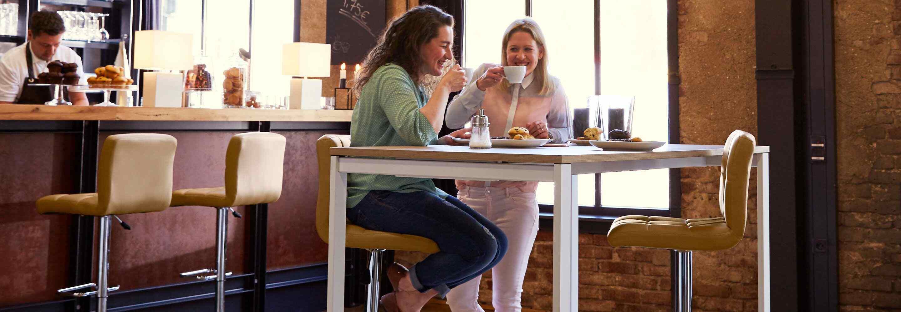 Twee vrouwen zitten te lachen in een café en drinken samen koffie.