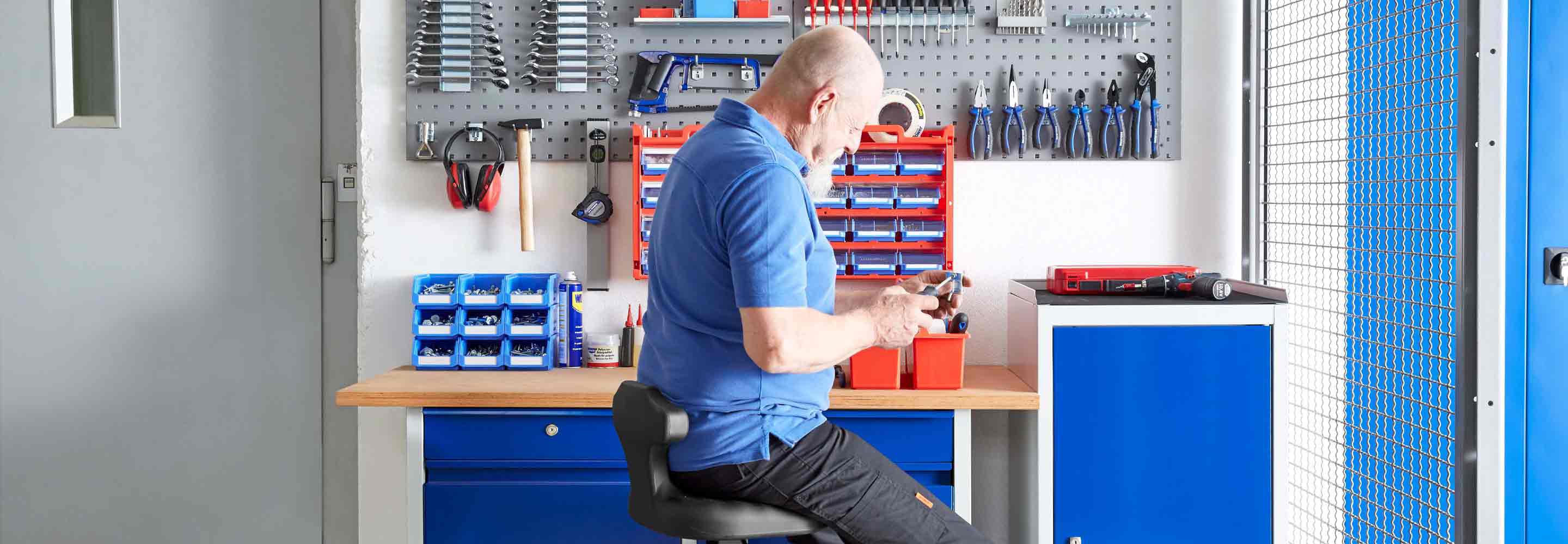 Een man zit in een werkplaats met gereedschap in zijn handen.