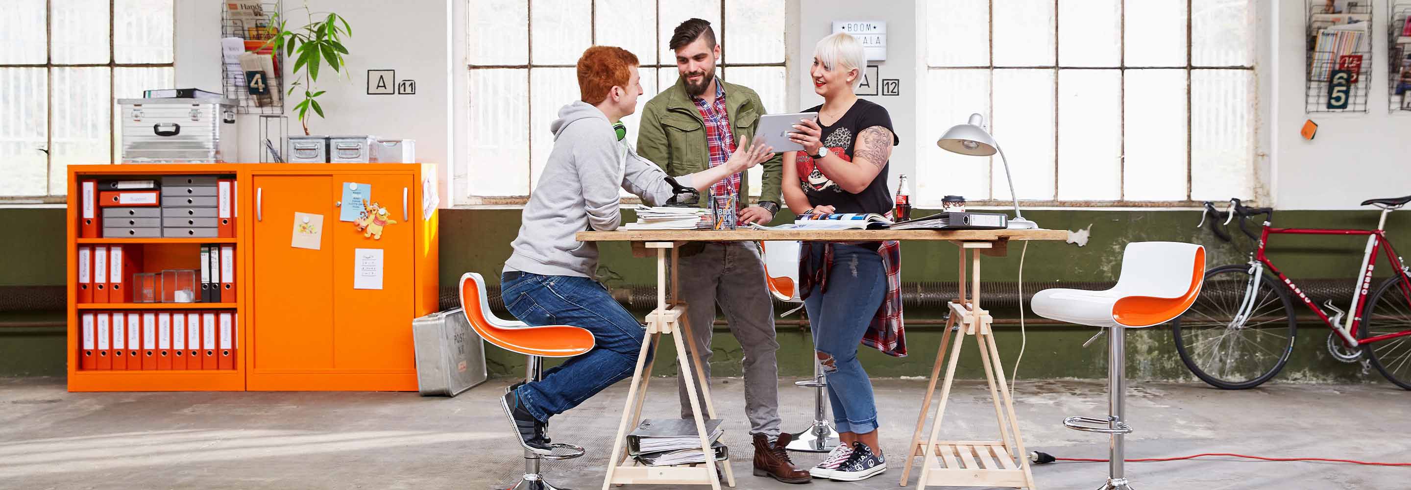 Drei Personen stehen an einem Tisch und sind dabei einen Workshop zu planen.