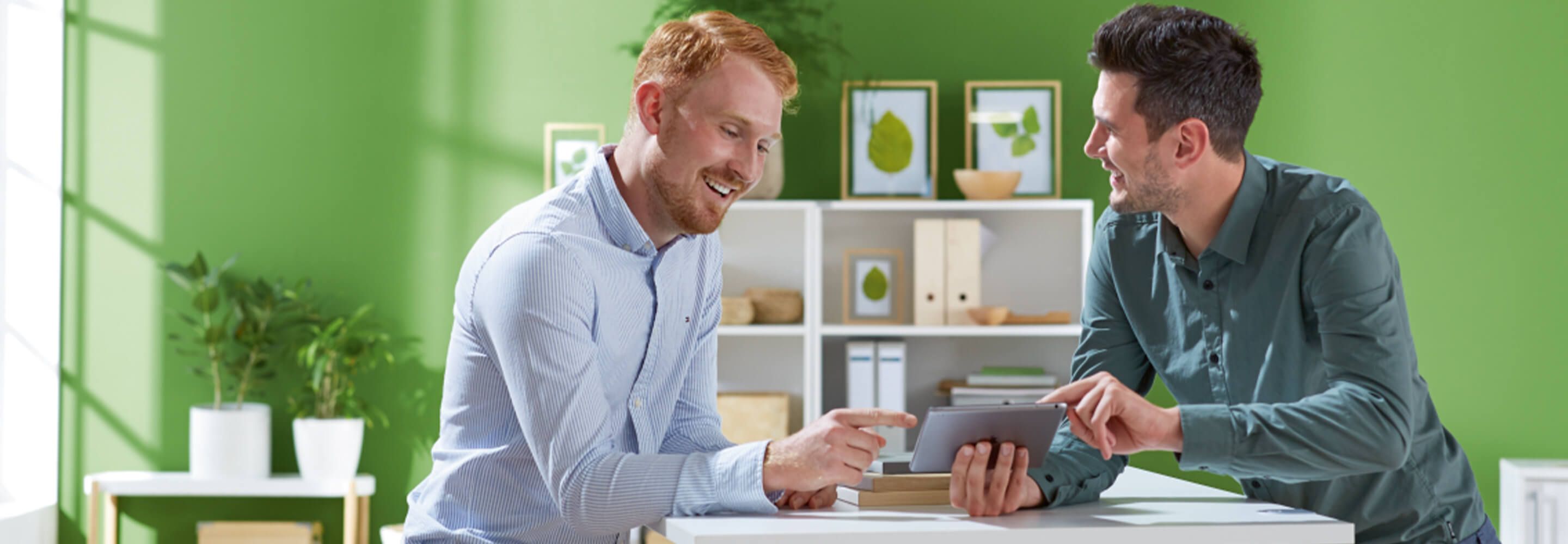 Twee mannen zitten tegenover elkaar, lachen en werken samen aan een project met de Kanban- of Scrum-methode.