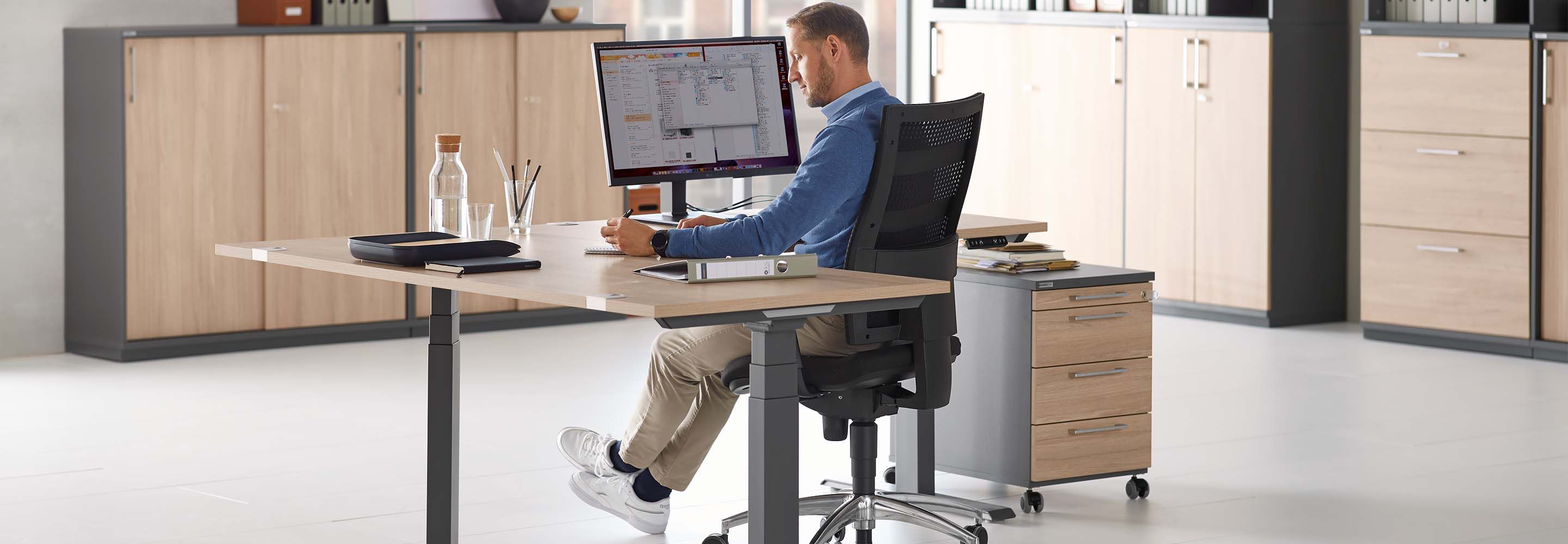 Een man zit aan zijn bureau in zijn kantoor en schrijft iets op.
