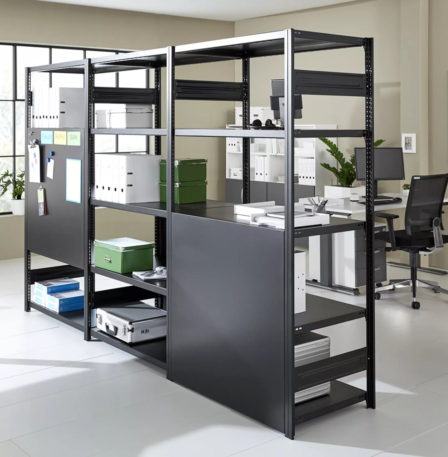 Schwarzes Regalsystem in einem Büro mit Schreibtisch, Bürostuhl und verschiedenen Aufbewahrungsboxen.