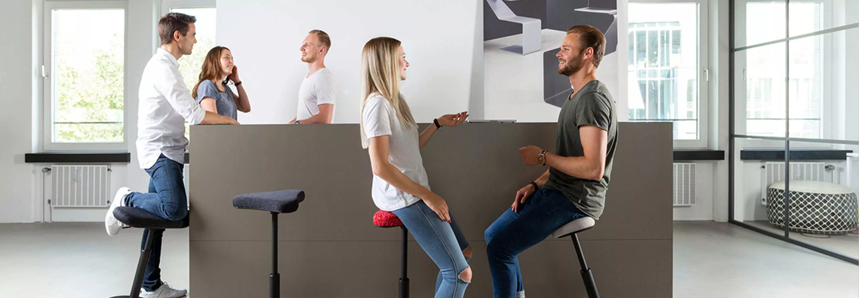 Fünf Personen im Büro, die sich stehend oder auf einem Arbeitshocker sitzend unterhalten
