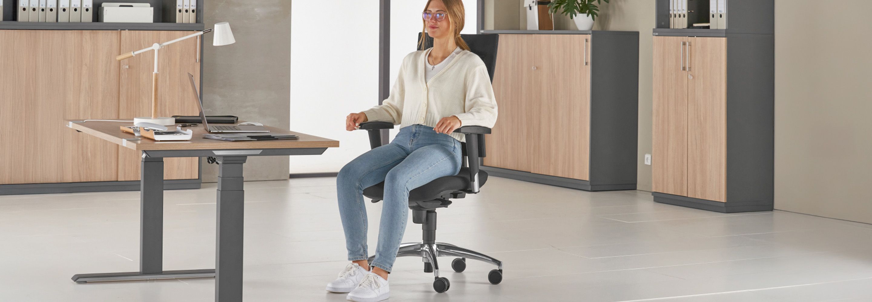 Junge Frau auf ergonomischem Bürostuhl in hellem Büro mit höhenverstellbarem Schreibtisch