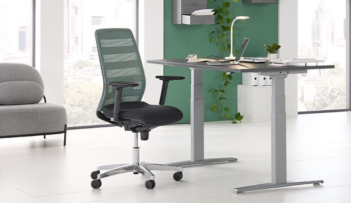 Ergonomischer Bürodrehstuhl vor elektrisch höhenverstellbarem Schreibtisch im Office