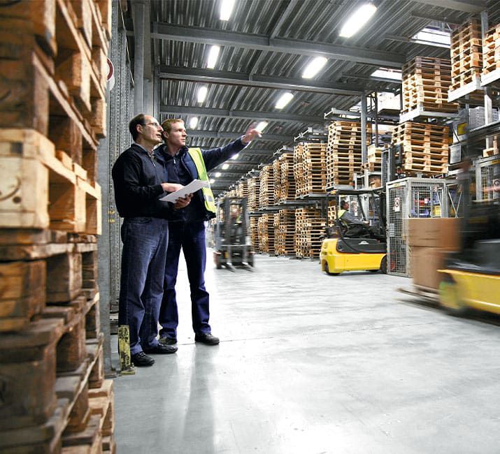 Mitarbeiter bespricht neue Lagervision zwischen hohen Palettenregalen und Gabelstaplern in moderner Halle