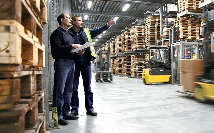 Mitarbeiter bespricht neue Lagervision zwischen hohen Palettenregalen und Gabelstaplern in moderner Halle