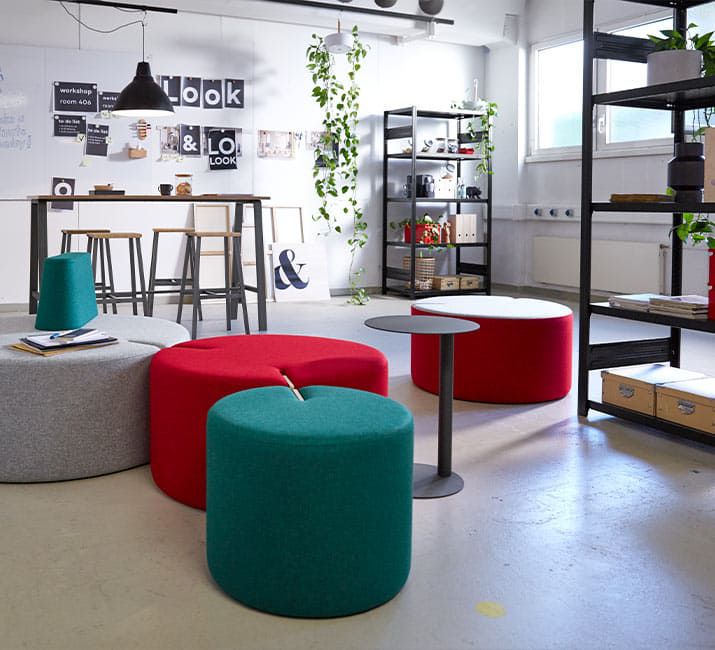 Bunte Loungemöbel und Hocker vor offenen Regalen mit Dekopflanzen in inspirierendem Arbeitsbereich