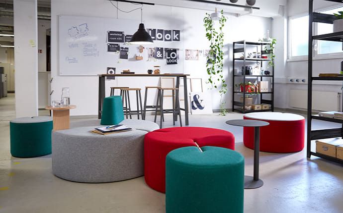 Bunte Loungemöbel und Hocker vor offenen Regalen mit Dekopflanzen in inspirierendem Arbeitsbereich