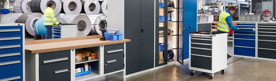 Industriearbeitsplatz mit Werkbänken, Werkzeugschränken und mobilen Rollcontainern in einer Produktionsumgebung