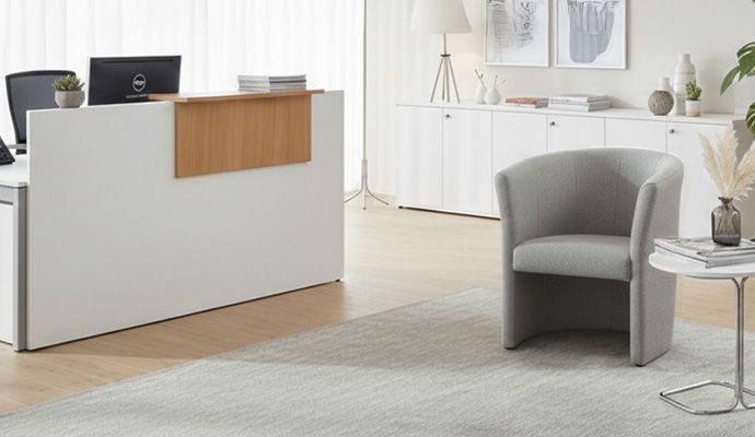 Modernes Wartezimmer mit Lounge-Sesseln, Empfangstresen und großem Display mit aktueller Wartezeit-Anzeige.