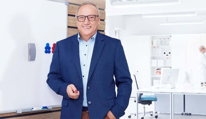 Ein Mann steht lächelnd vor einem Whiteboard in einem Büro.