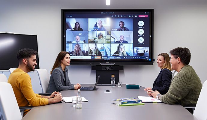 Vier Personen in einem modernen Konferenzraum bei einem Videomeeting