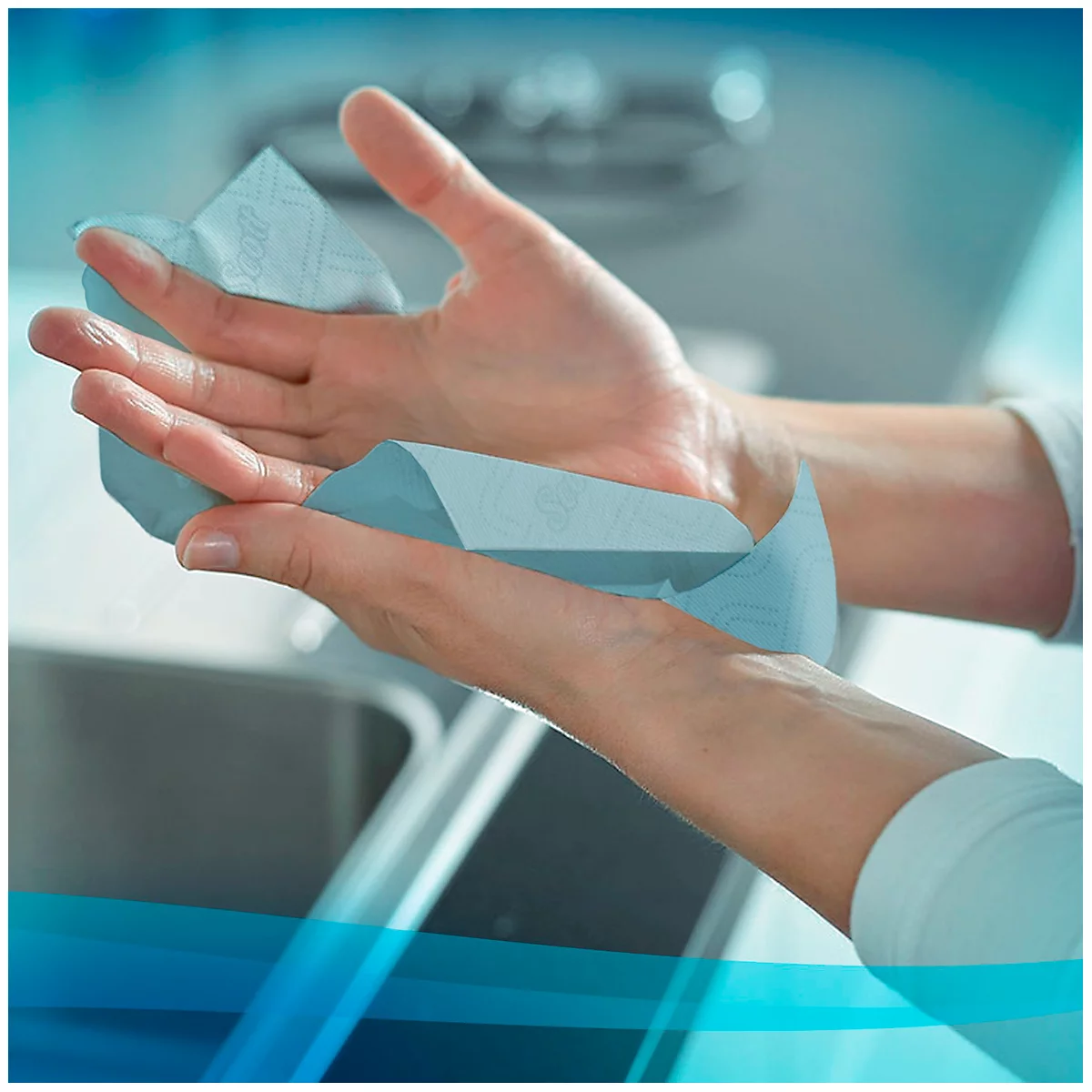 Manos secándose con una toalla de papel azul sobre un lavabo.