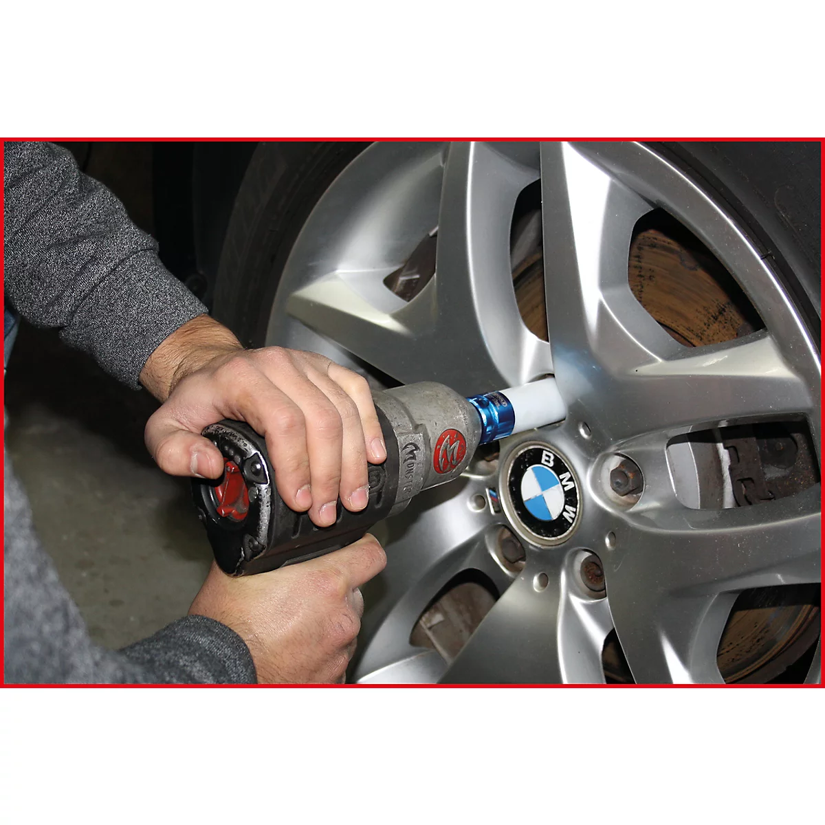 Jemand schraubt mit einem Schlagschrauber an einem Autoreifen. Das BMW-Logo ist sichtbar.