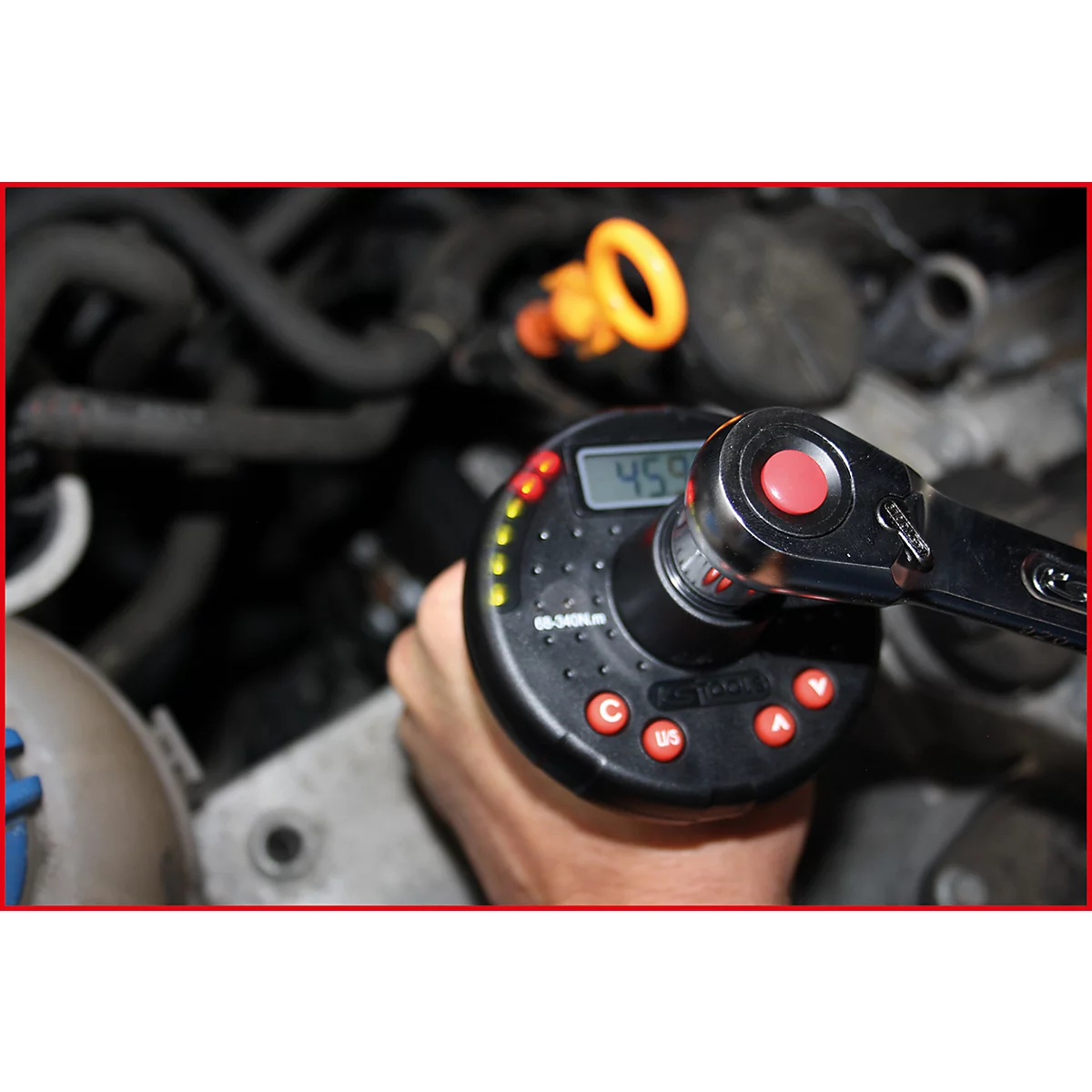 Mechaniker mit elektronischem Drehmomentschlüssel beim Schrauben in einem Motorraum. Auf dem Display ist 459 angezeigt.