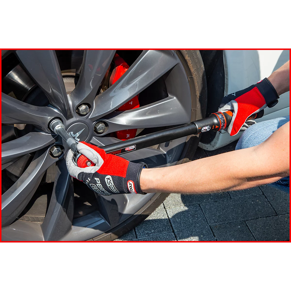 Person wechselt Reifen an einem Tesla. Mit rotem Handschuh wird die Radmutter mit einem Drehmomentschlüssel gelöst.