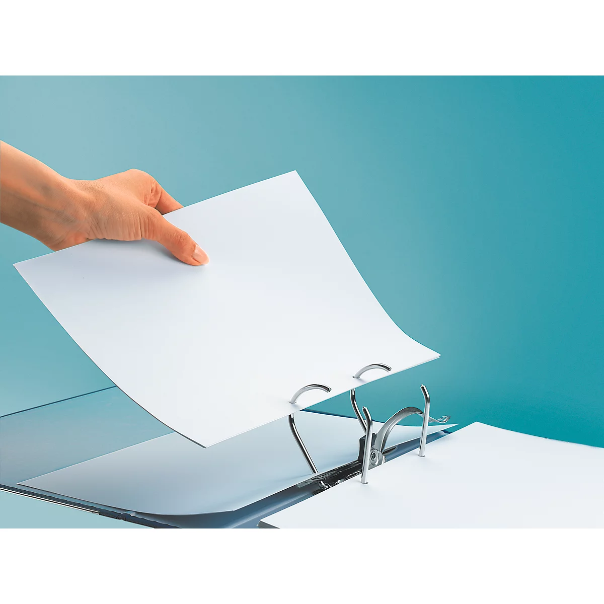 A hand inserts a white sheet of paper into a binder, which lies on a blue background.