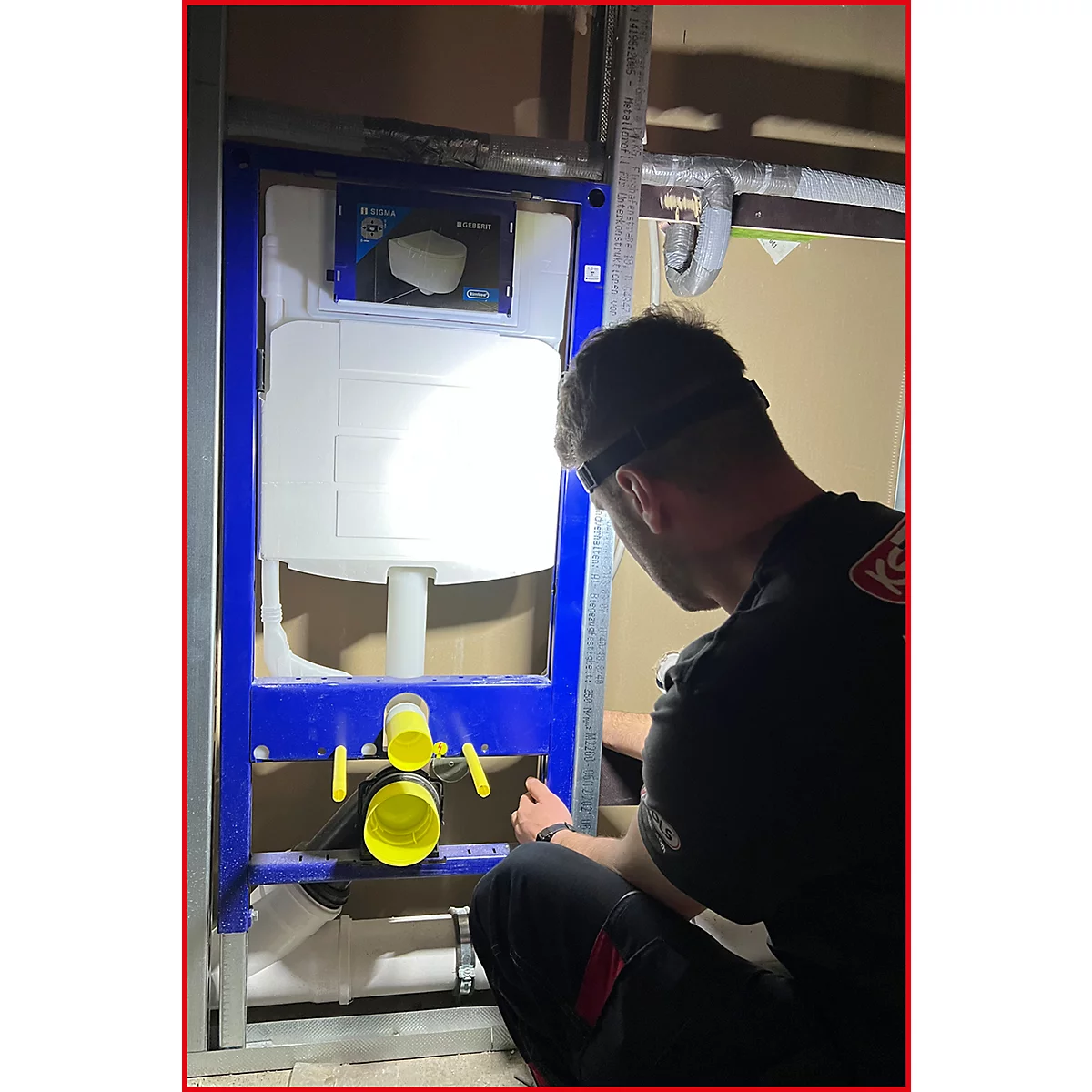 Ein Mann in Arbeitskleidung montiert eine WC-Vorwandinstallation. Blaue Halterung, weißer Spülkasten, gelbe Anschlüsse.