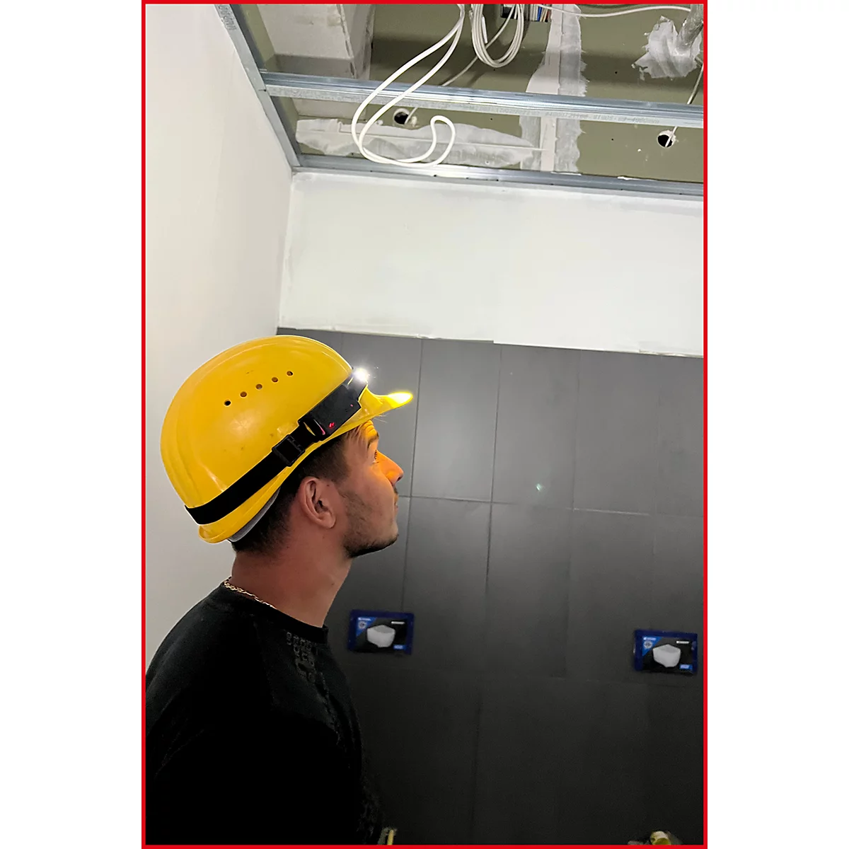 Ein Mann mit gelbem Helm und Stirnlampe blickt an die Decke. Er steht vor einer grauen Wand.