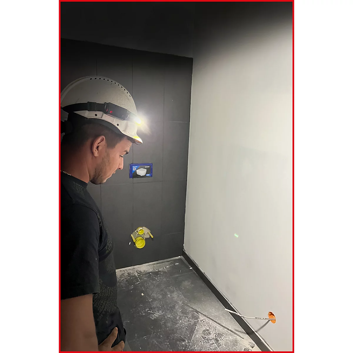Ein Arbeiter mit Helm und Stirnlampe betrachtet konzentriert eine Baustelle in einem Badezimmer.