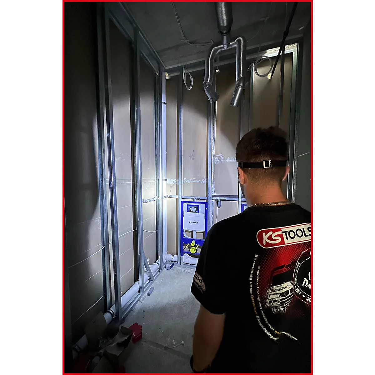 Ein Mann betrachtet einen Rohbau. Im Hintergrund sind Sanitärinstallationen und ein Kasten für die Toilettenspülung zu sehen.