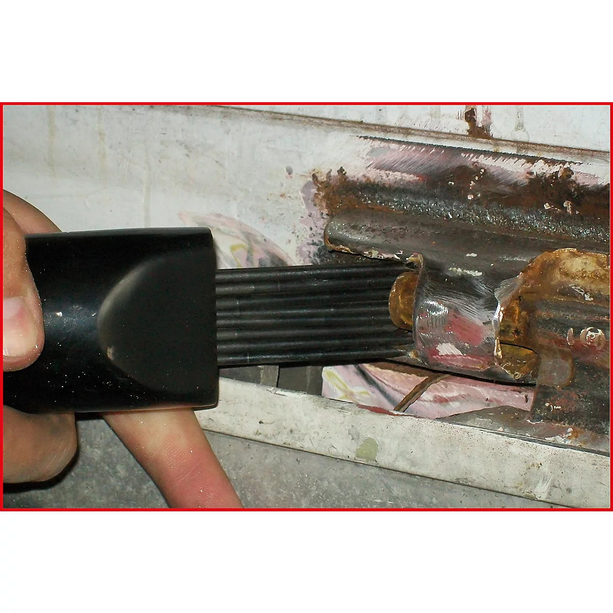 Nahaufnahme einer Hand, die ein Werkzeug in ein rostiges Metallteil einführt. Schwarzes Werkzeug, metallische Elemente mit Rost.
