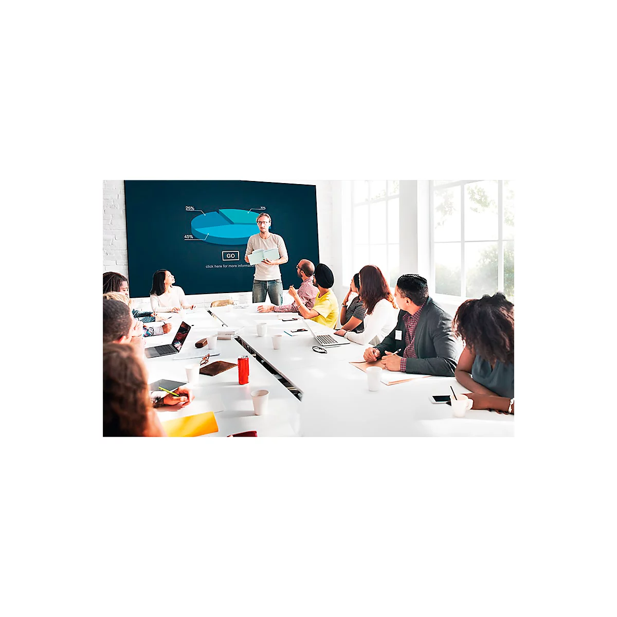 A man presents a graphic in a meeting. A group of colleagues sit at a table and listen.