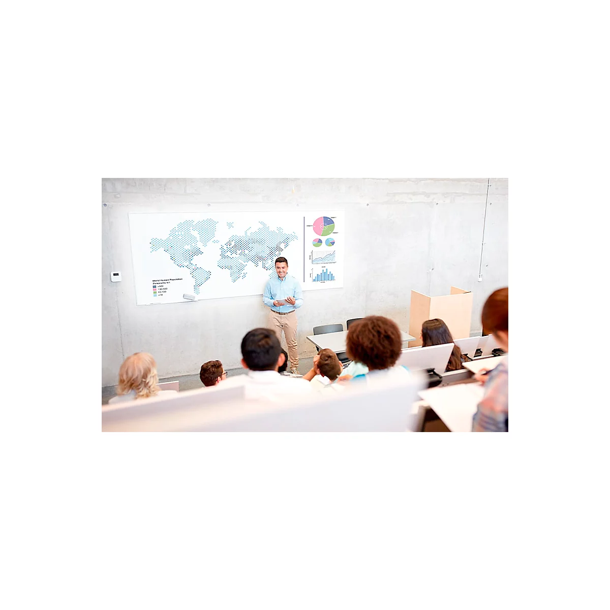 A man presents to a class. A world map and diagrams are visible on the wall. Students are listening attentively.