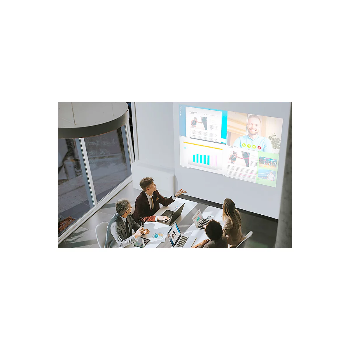 Team meeting with presentation and video. A person is standing and explaining something. Others are sitting at laptops.