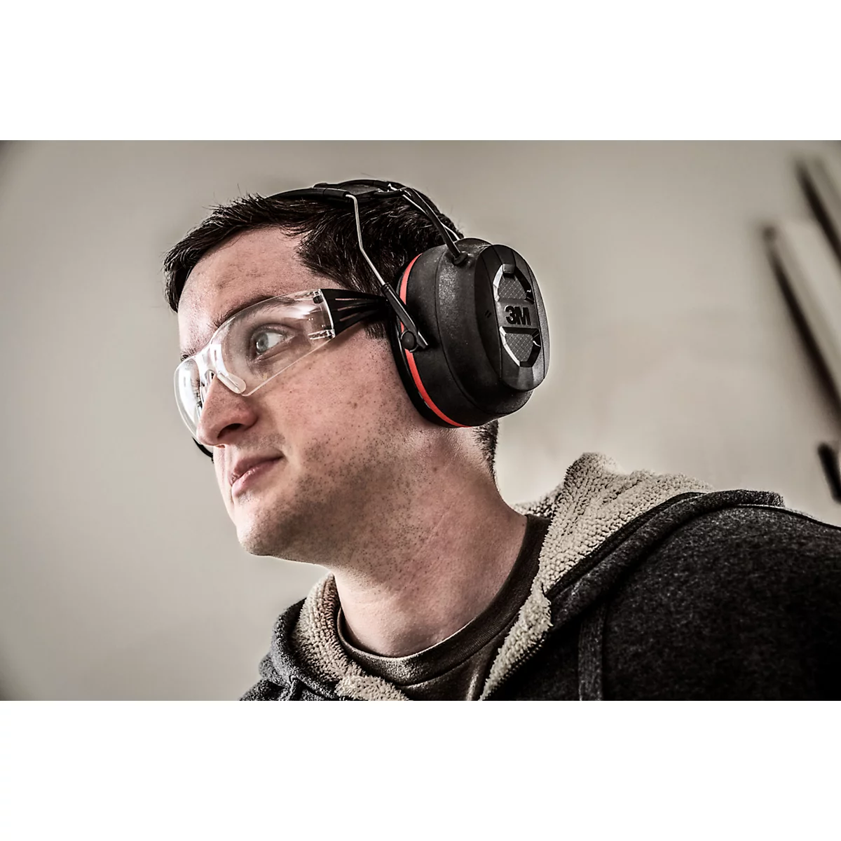 Ein Mann mit Schutzbrille und Gehörschutz schaut zur Seite. Er trägt einen Hoodie.