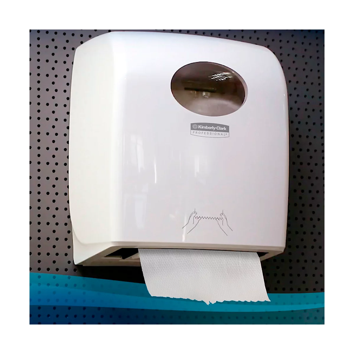 Witte papieren handdoekdispenser op grijs geperforeerd plaatstaal. Papier wordt uitgenomen. Logo 'Kimberly-Clark Professional'.