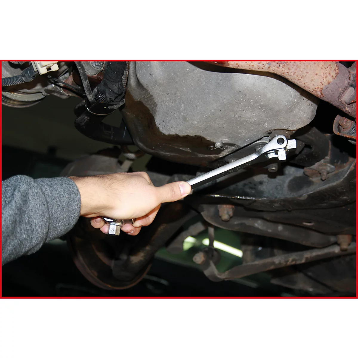 Ein Mann arbeitet unter einem Auto und benutzt einen Schraubenschlüssel, um eine Schraube zu lösen.