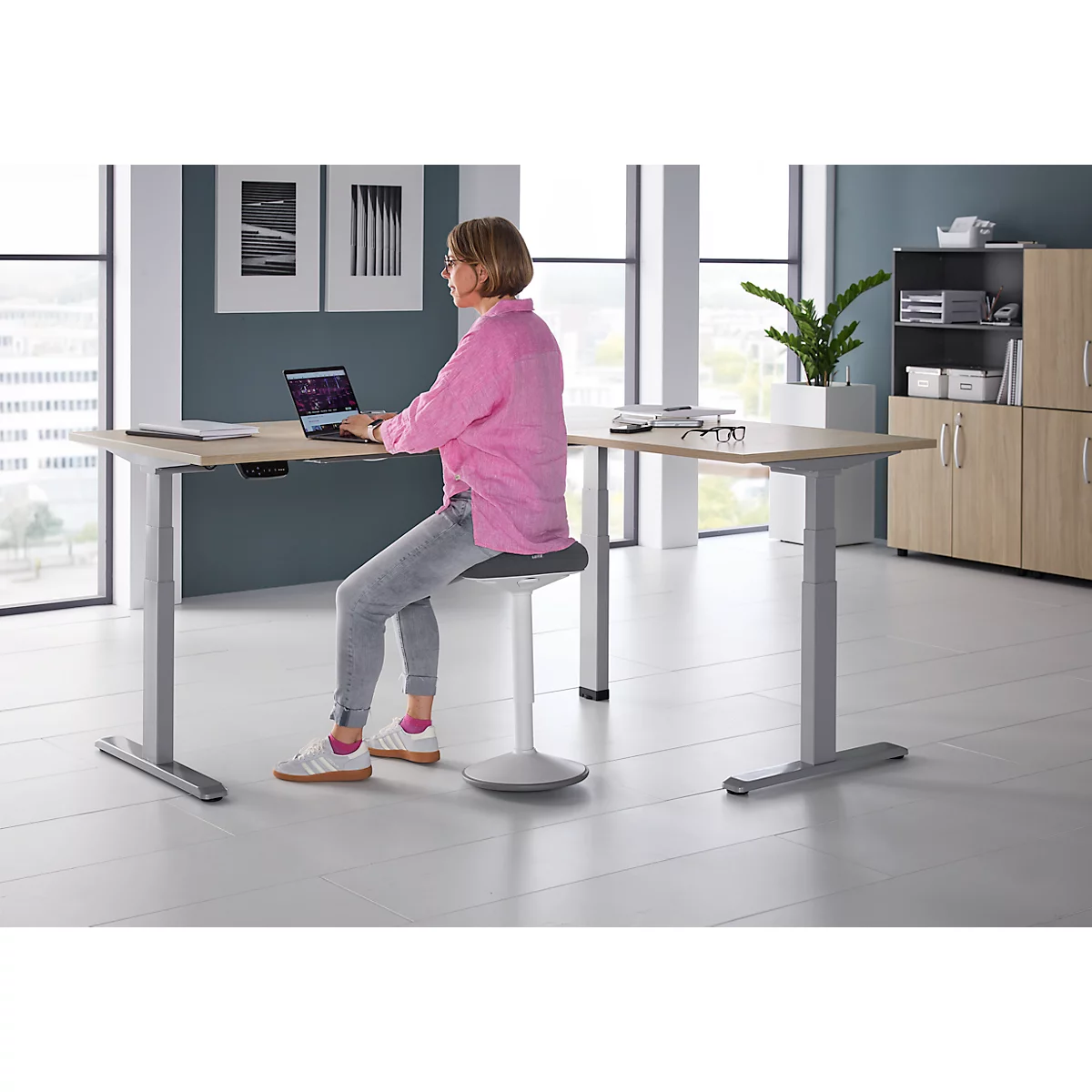 Een vrouw zit aan een in hoogte verstelbaar bureau en werkt op een laptop.