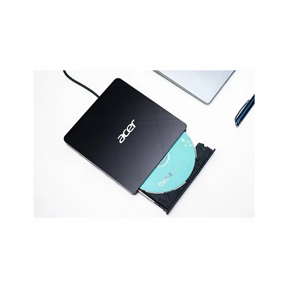 Schwarzes externes Acer DVD-Laufwerk mit eingelegter blaugrüner DVD-R auf weißem Schreibtisch.