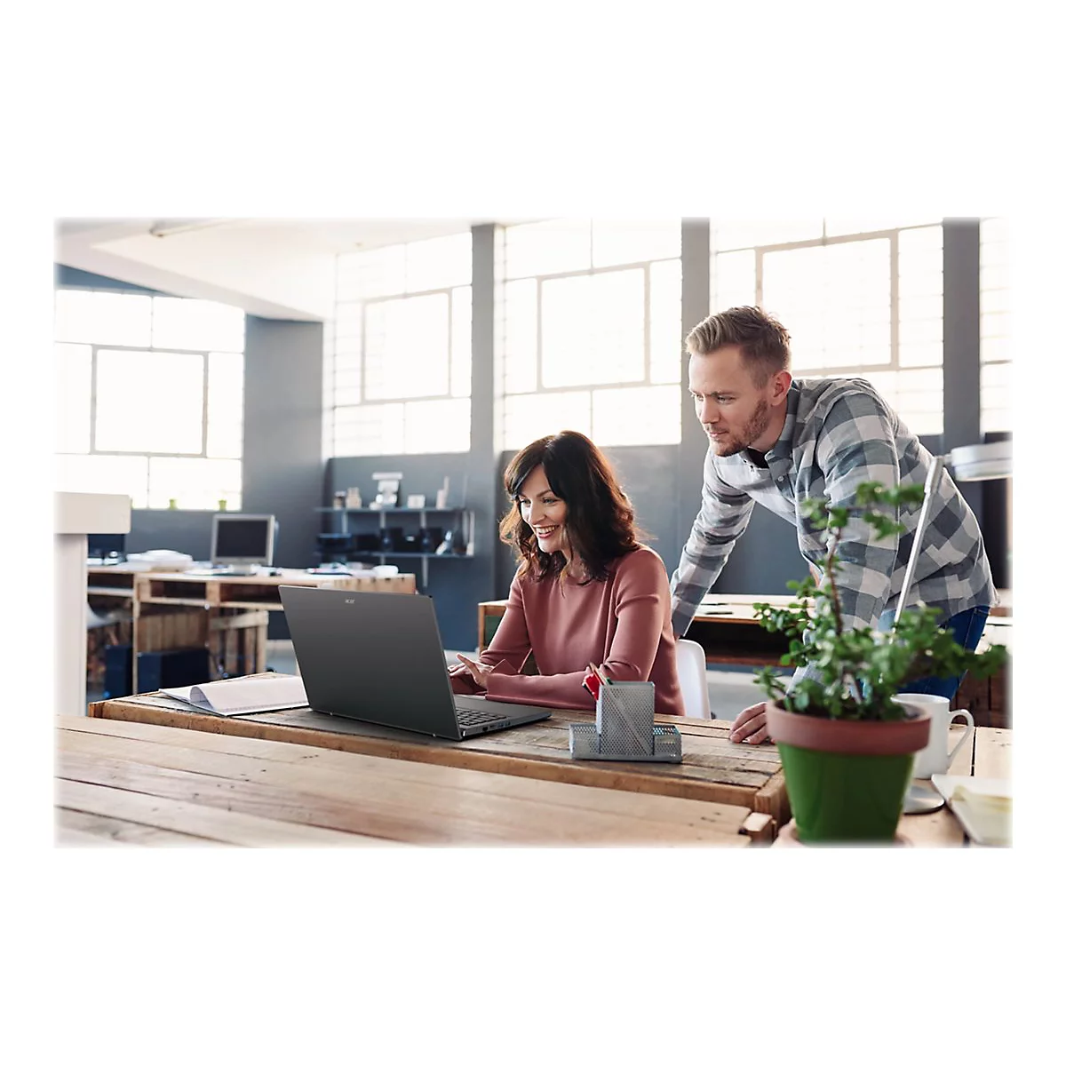 Eine Frau und ein Mann arbeiten gemeinsam an einem Laptop an einem Holztisch. Die Frau lÃ¤chelt.