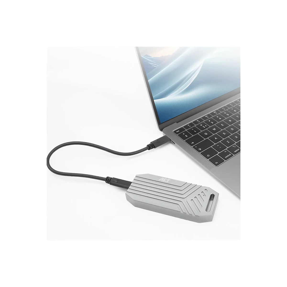 Eine graue externe SSD mit ACT-Logo ist über ein schwarzes USB-Kabel mit einem silbernen Laptop verbunden.